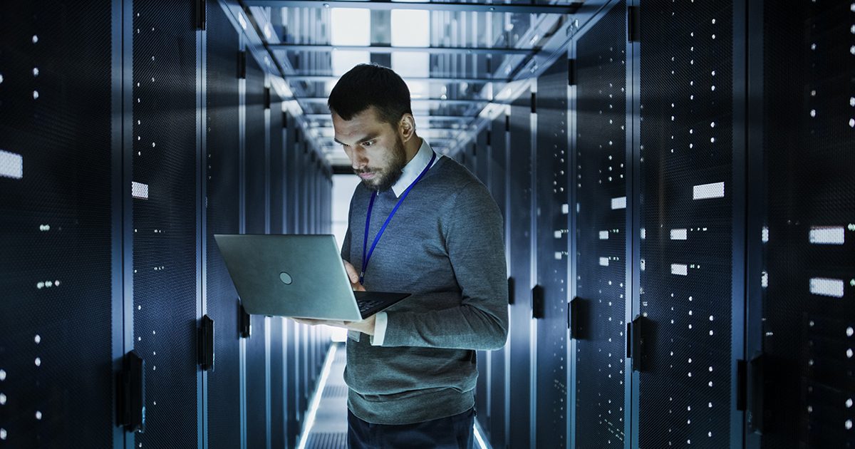 IT professional in server room looking at laptop