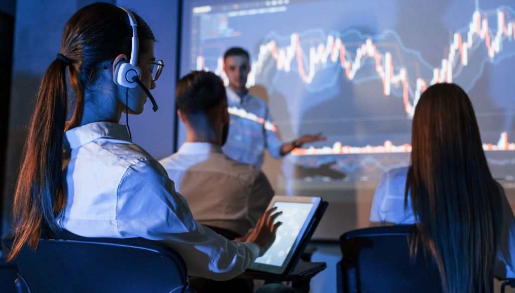 Woman using digital tablet. Male leader talking to employees, showing the plan on the projector in office of a financial company.