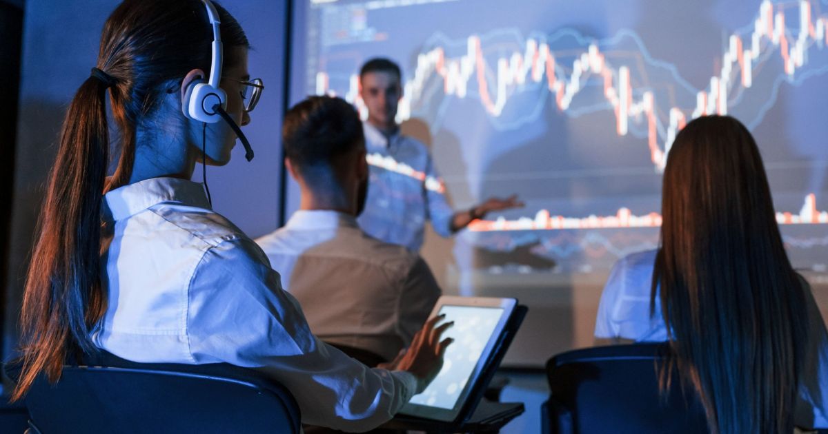 Woman using digital tablet. Male leader talking to employees, showing the plan on the projector in office of a financial company.