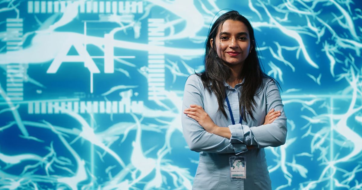 Portrait of smiling IT specialist standing with arms crossed in front of cutting edge display featuring AI and neural network graphics. Researcher in startup doing advancements in AI field, camera A