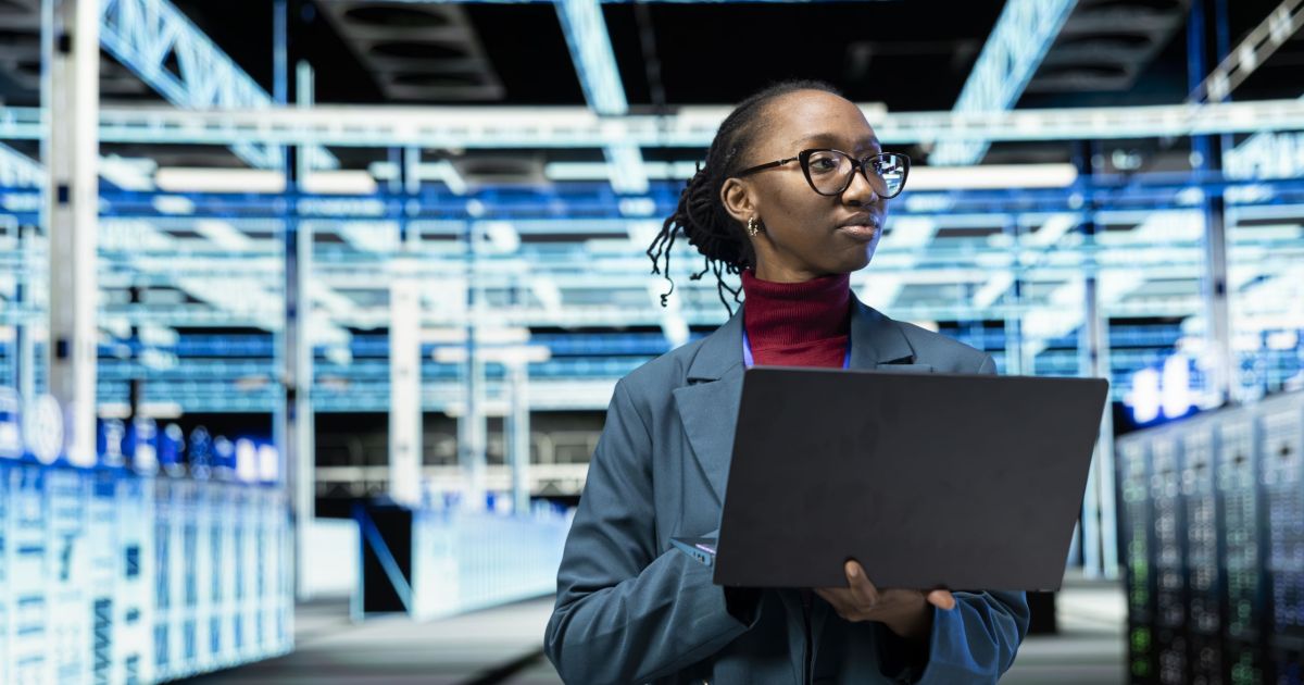 Data center female technician uses laptop program in data center