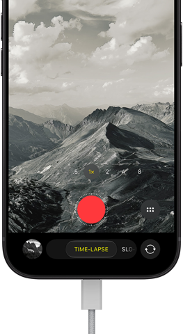 iPhone 18 Pro, front exterior, displaying a mountainous landscape, with the camera mode overlay in Time-Lapse mode, with charging cable attached to charging port