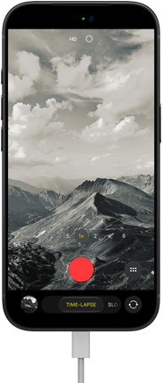 iPhone 18 Pro, front exterior, displaying a mountainous landscape, with the camera mode overlay in Time-Lapse mode, with charging cable attached to charging port